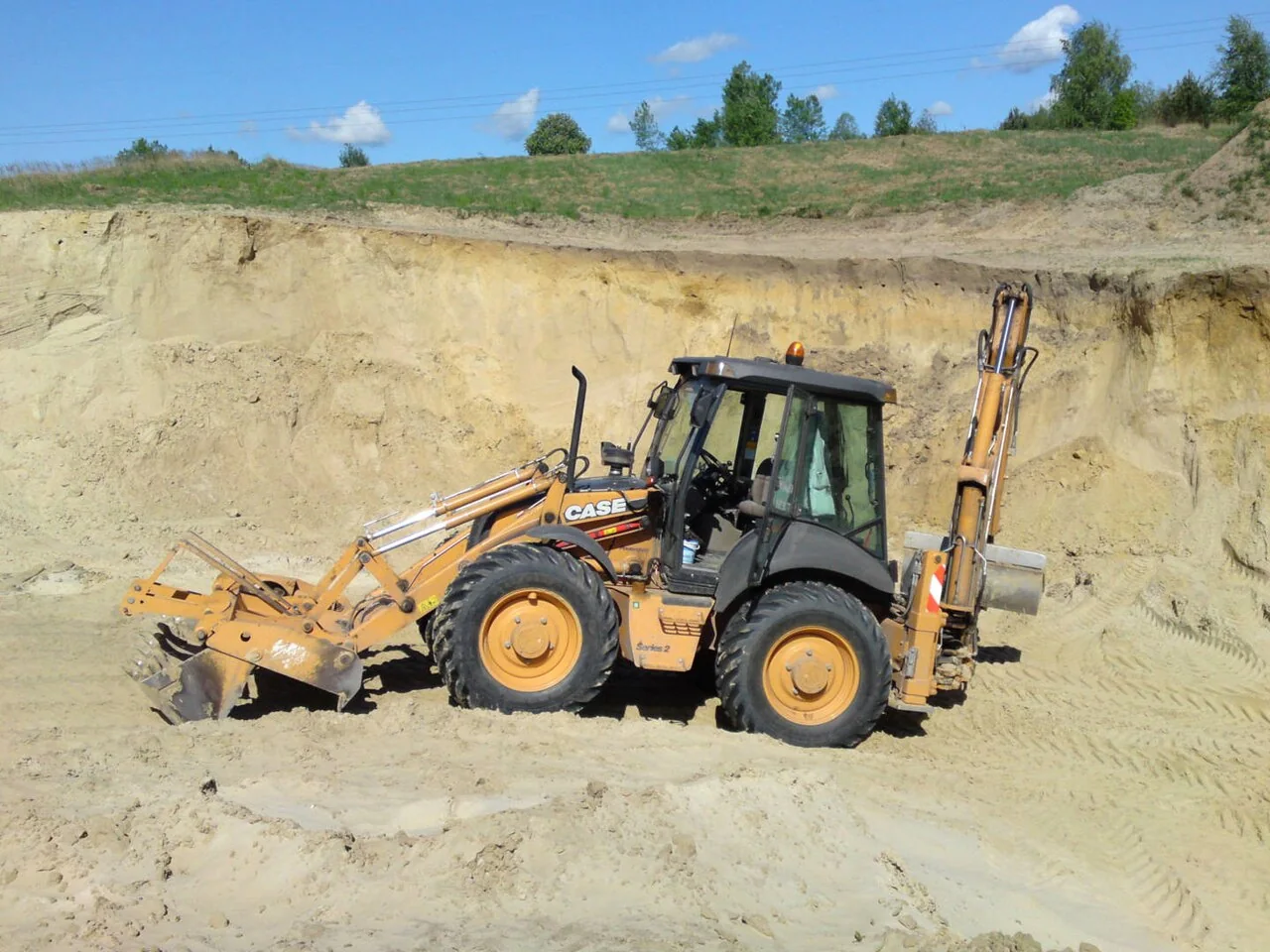 A yellow backhoe loader has a front bucket and a rear digging arm.