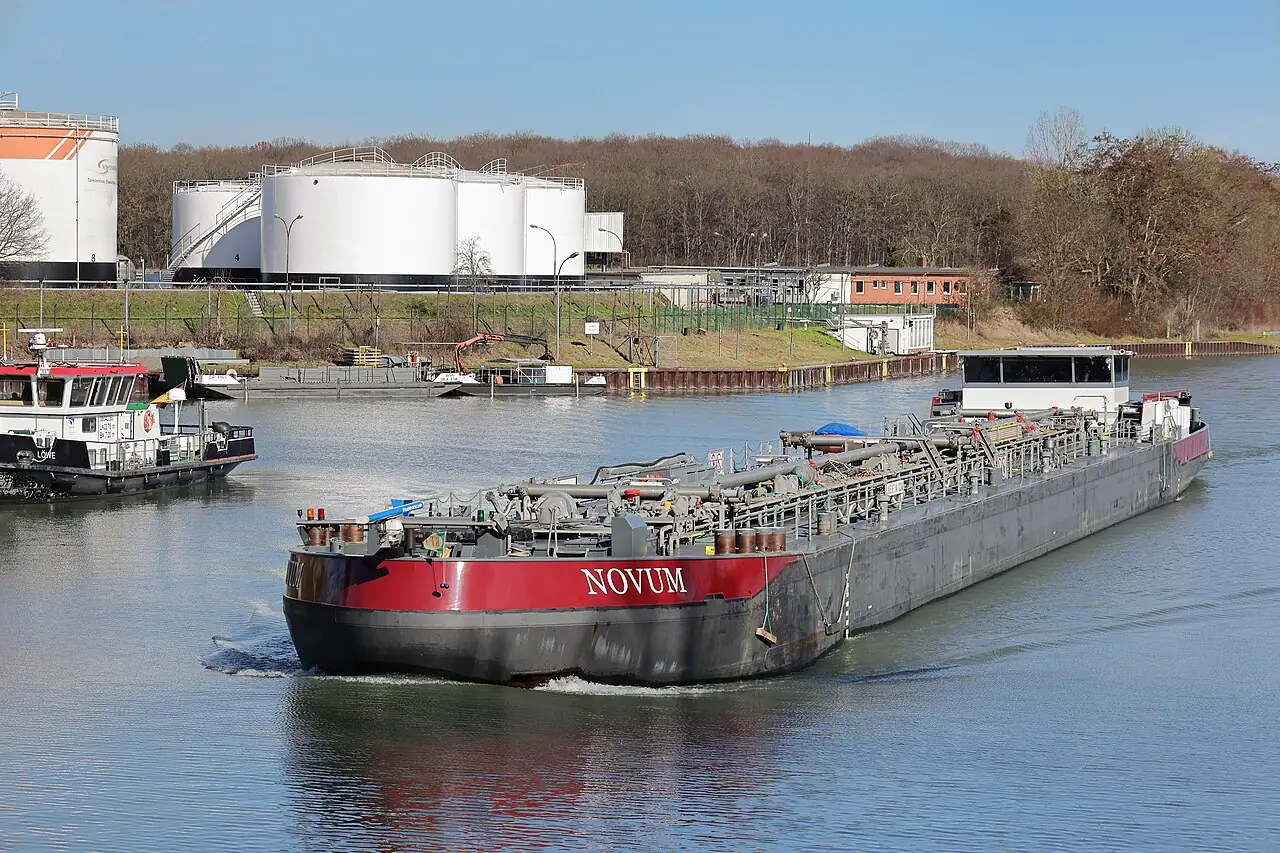 A long low cargo barge travels along a canal.