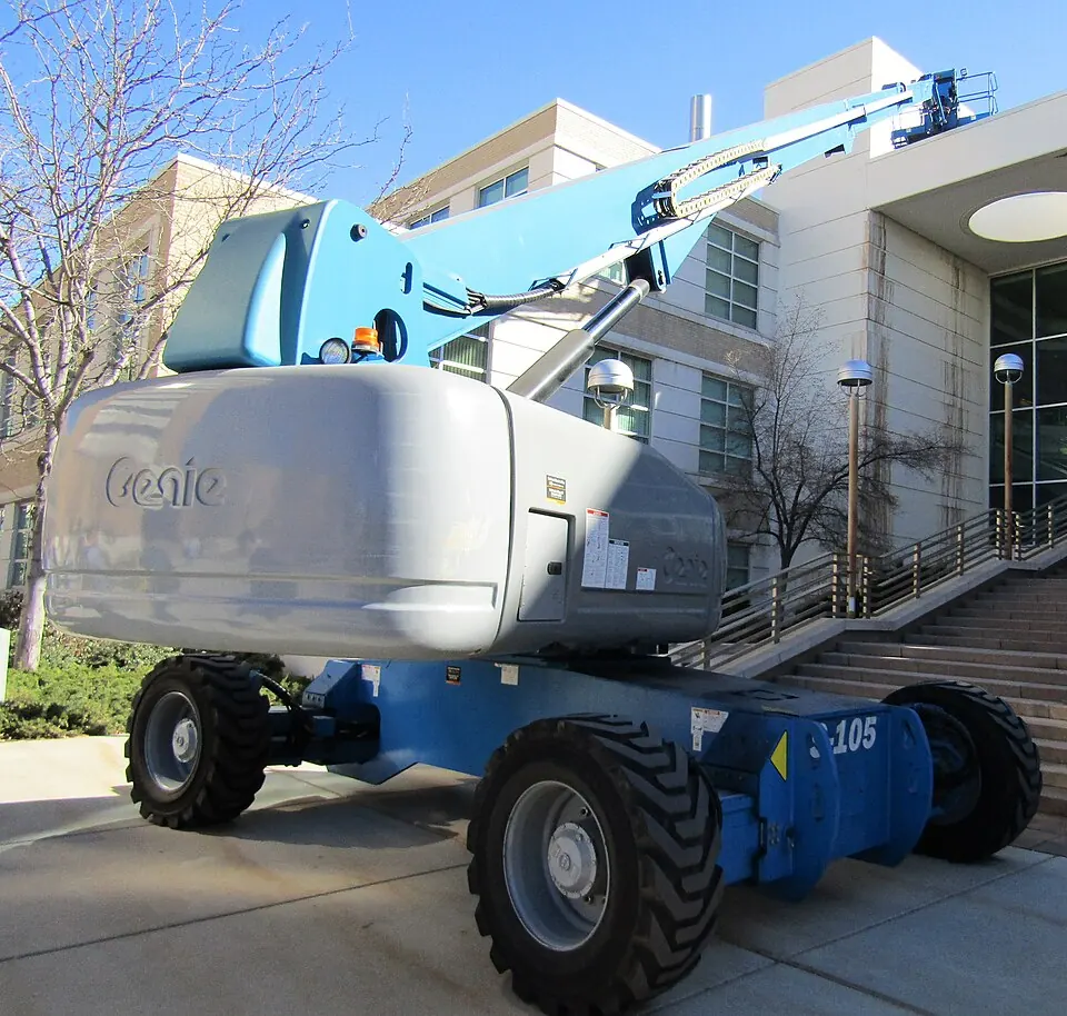 A blue-and-white boom lift raises its long arm beside a building.