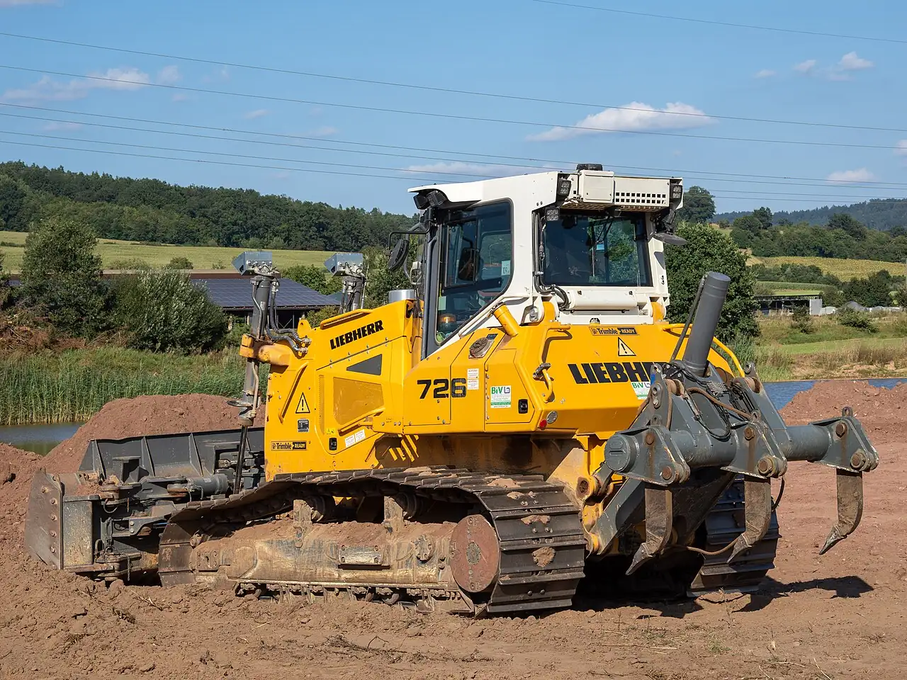 A yellow tracked bulldozer has a front blade and rear teeth.