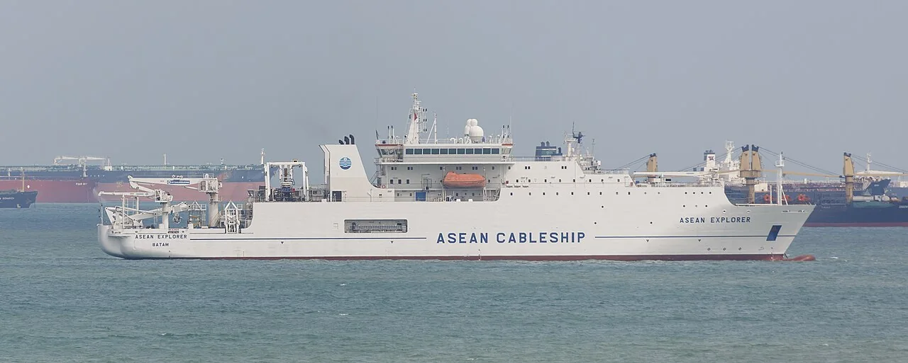 A white cable-laying ship has a tall bridge above its long working deck.