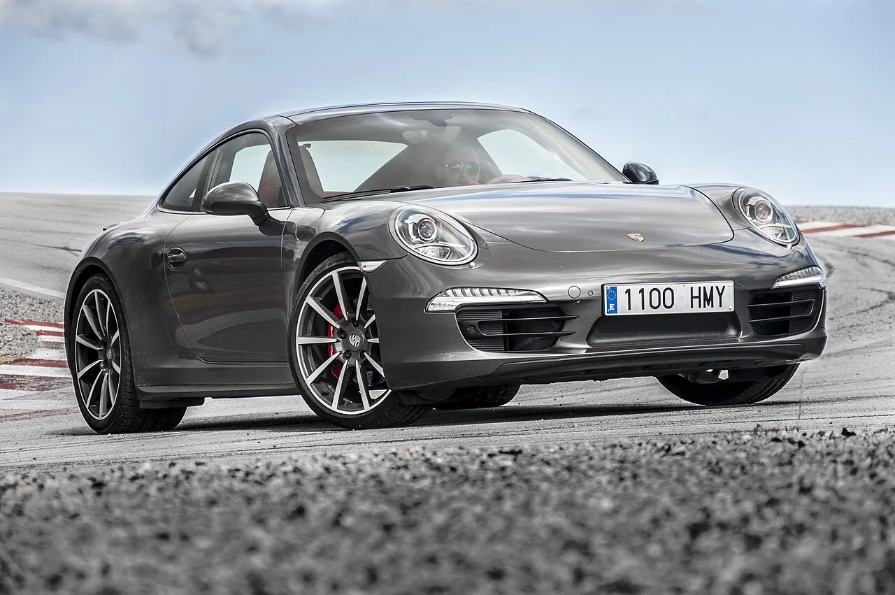 A grey sports car is shown from the front and side on a paved track.