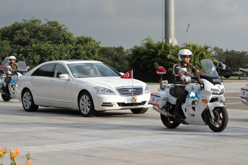A white car travels beside white police motorcycles on an open road.