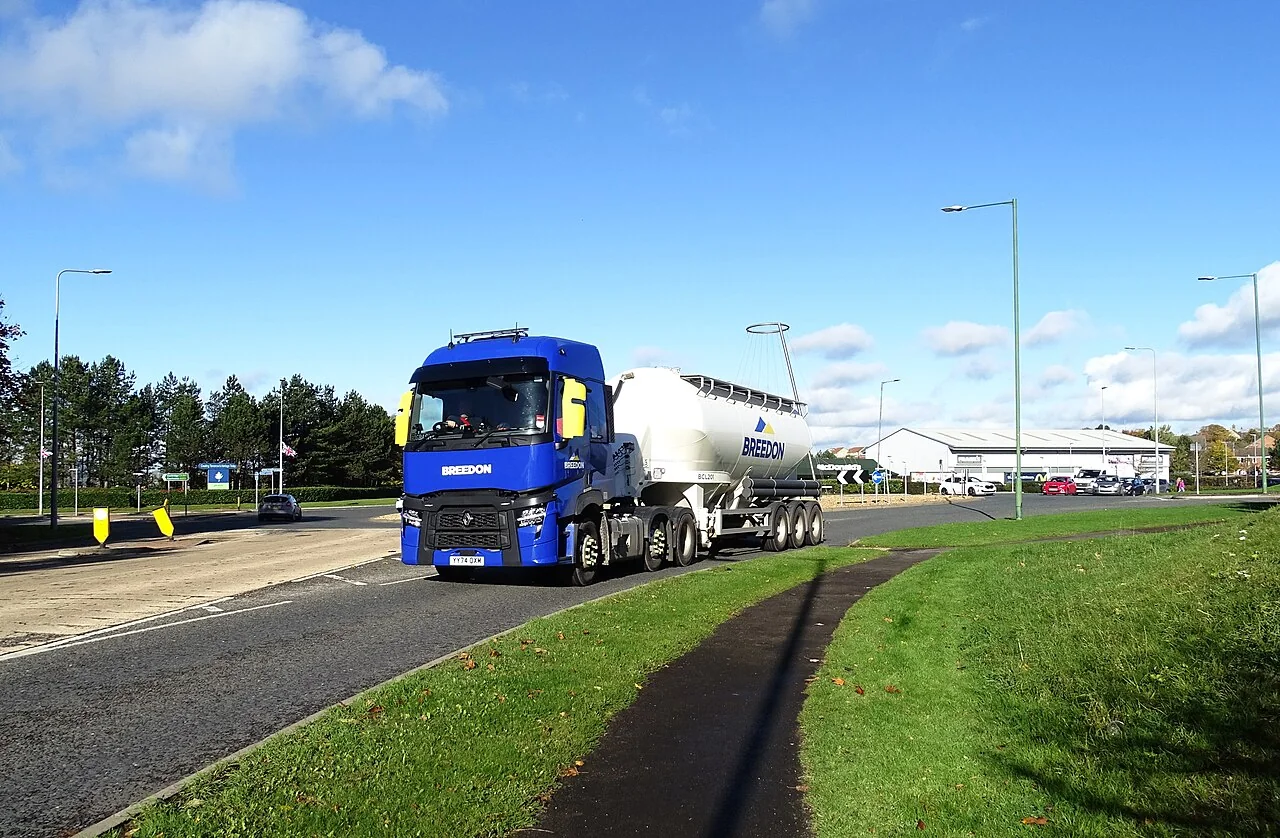 A blue truck pulls a white cement tanker trailer along a road.