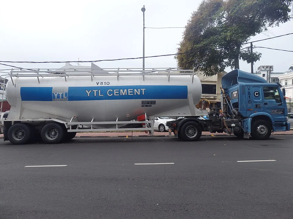 A blue truck pulls a long silver tank marked with the word CEMENT.
