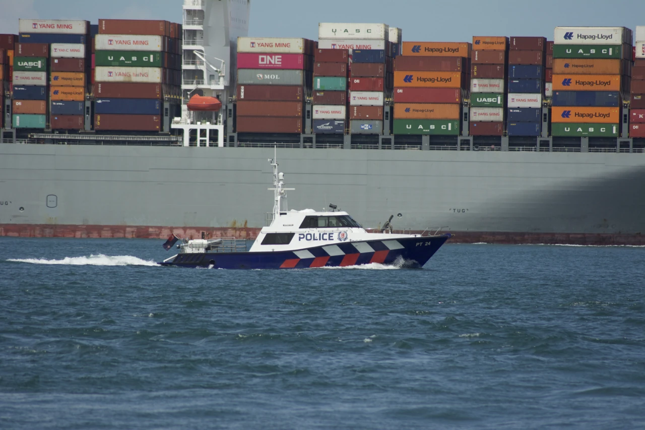 A small blue-and-white police boat passes beside a huge container ship.