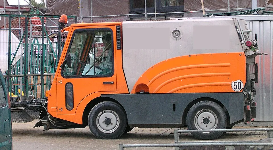 An orange-and-white compact sweeper has a tall box-shaped body and small wheels.