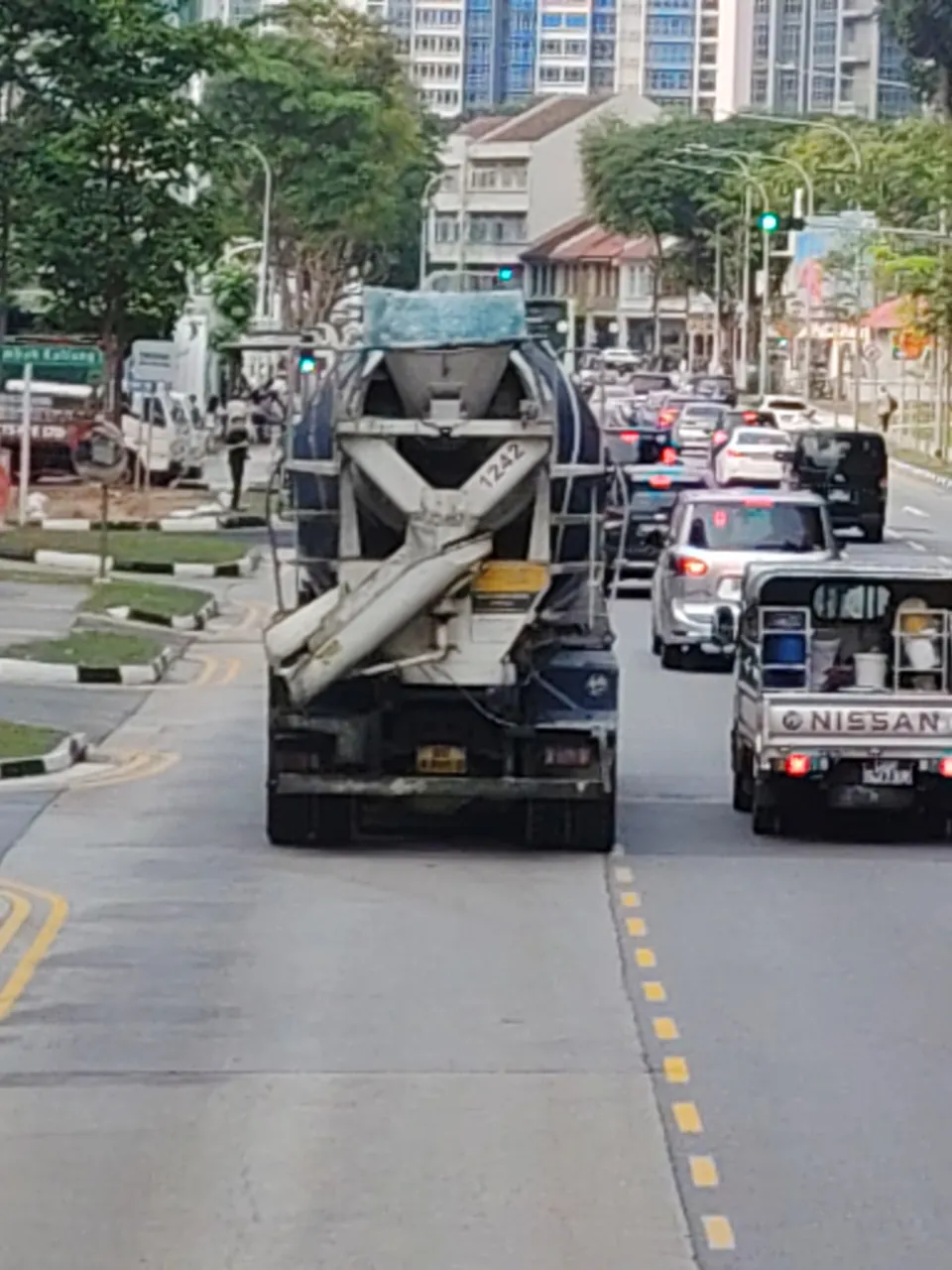 The rear of a mixer truck shows its ribbed drum, hopper and folded chute in traffic.