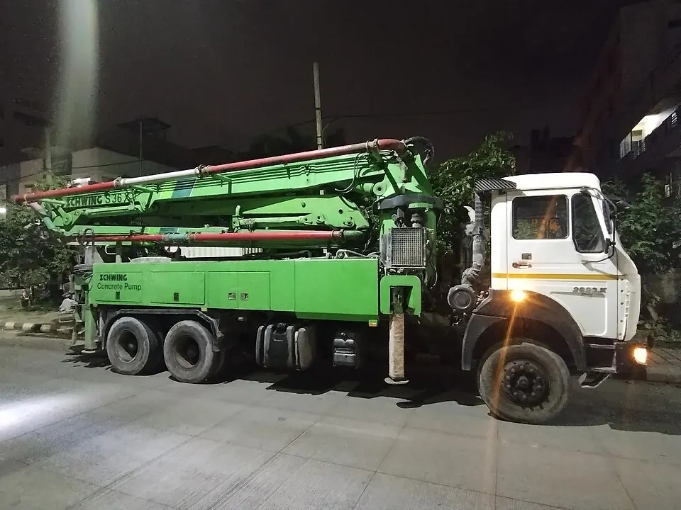 A white truck carries a green pumping arm folded above its rear wheels.