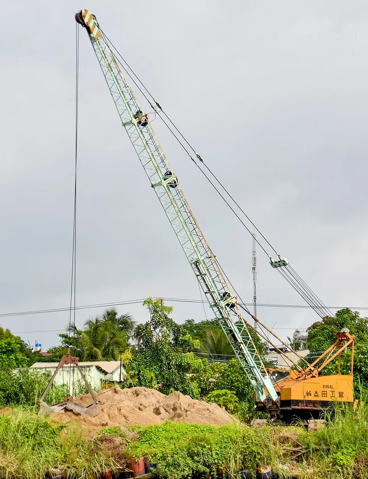 A tracked crane has a long green lattice boom pointing into the sky.