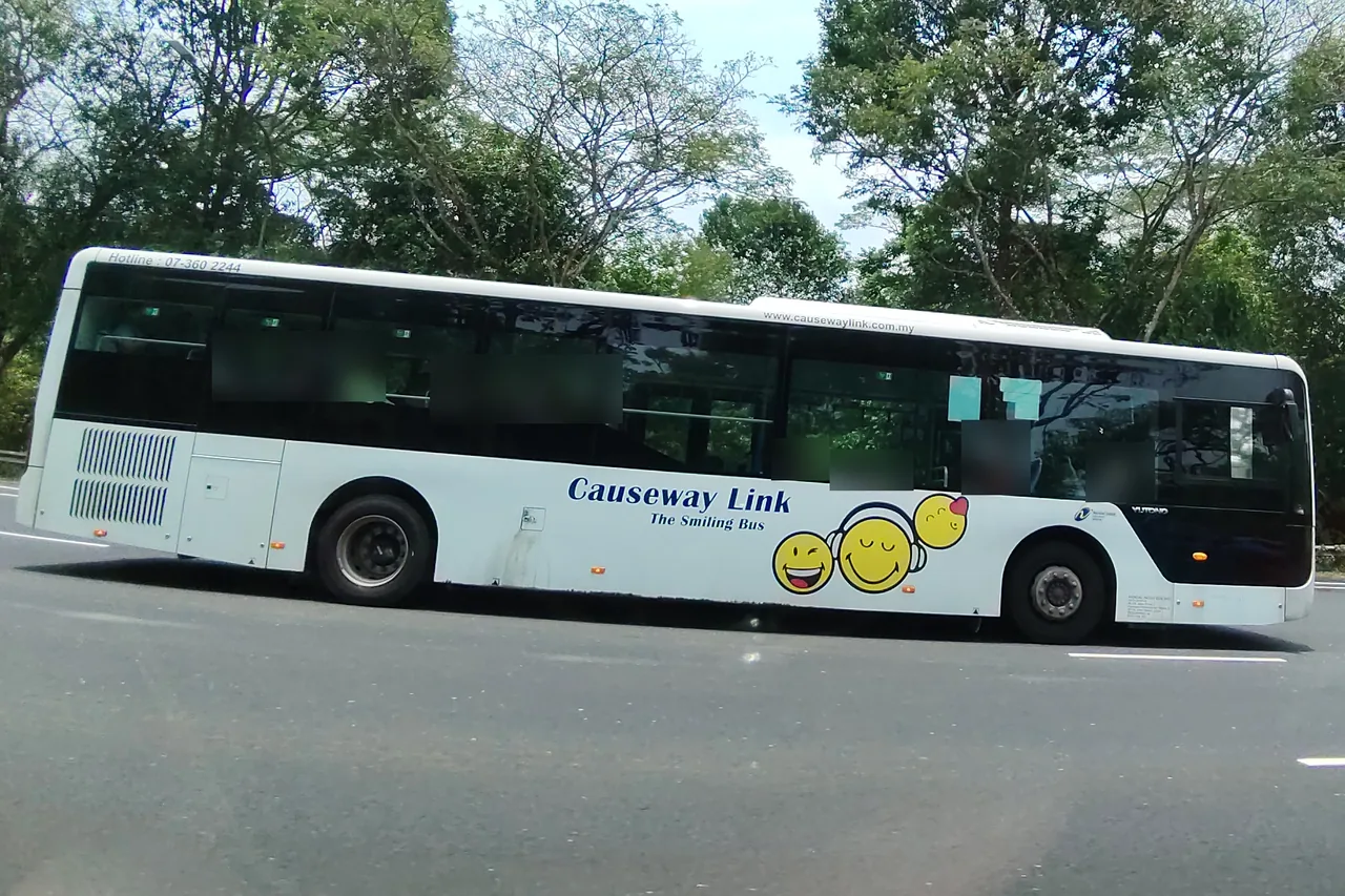 Cross-border bus — a white single-deck bus with three yellow smiley faces painted on its side, Photographed in Singapore