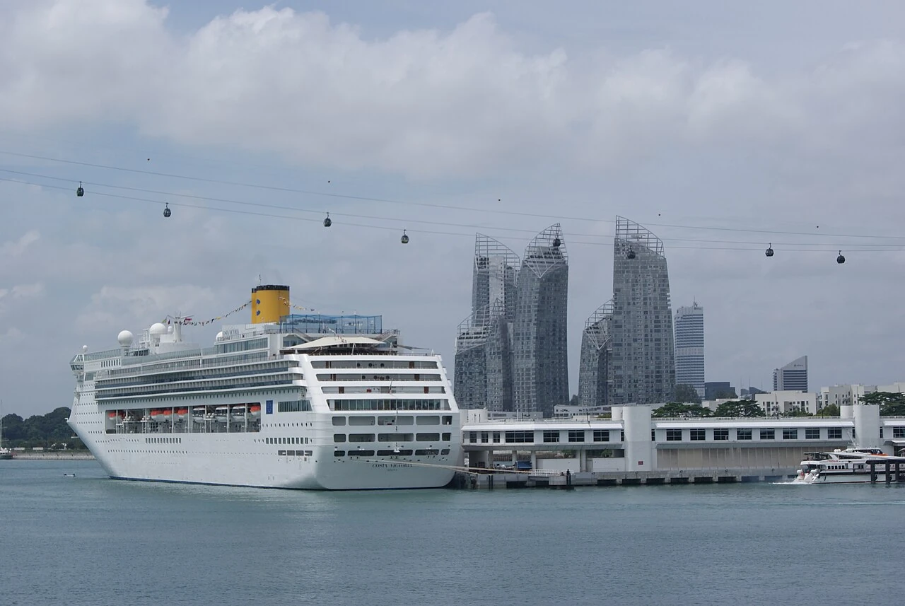 A large white cruise ship has many rows of windows and a yellow funnel.