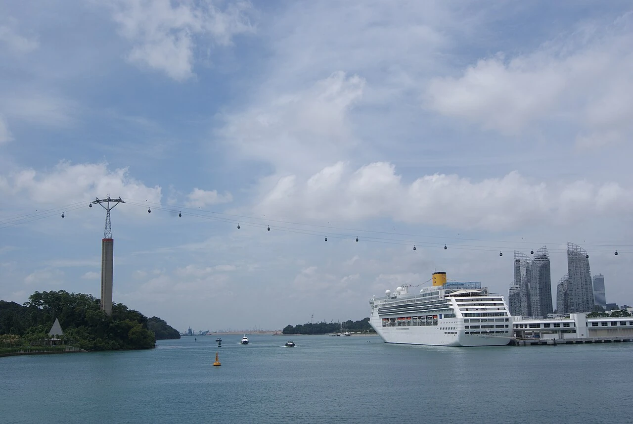 A white cruise ship stands beside a waterfront terminal beneath a cloudy sky.