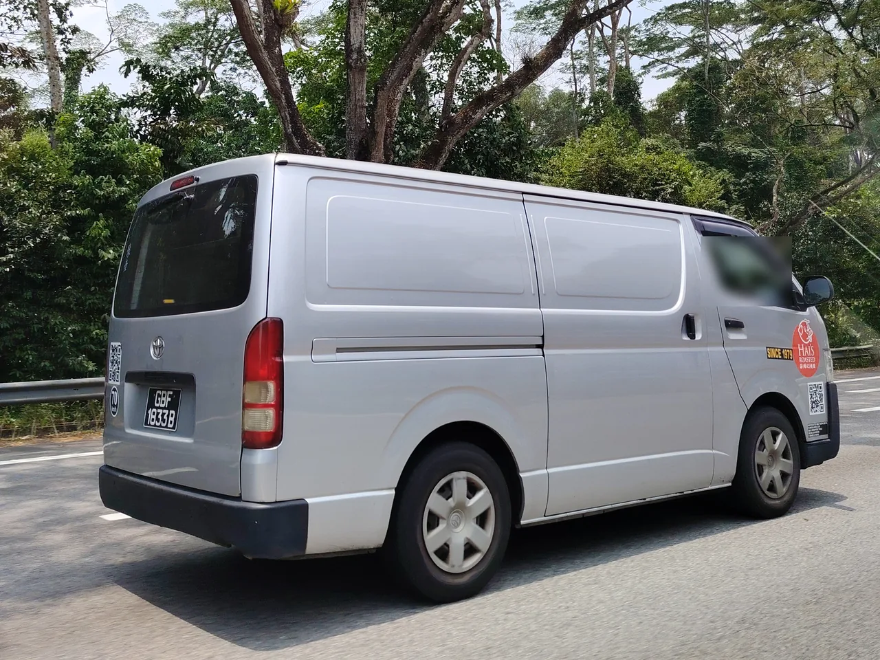 Delivery van — a silver delivery van seen from behind on a road with tall trees, Photographed in Singapore