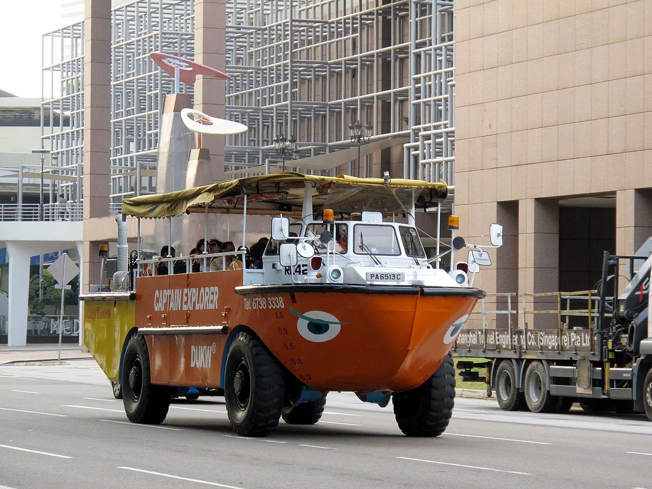 An orange amphibious tour vehicle carries passengers along a road.