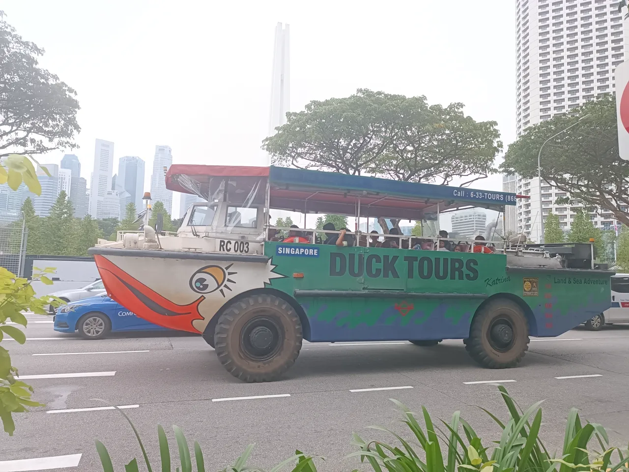 A green amphibious tour vehicle has large wheels and a duck's face painted on its front.