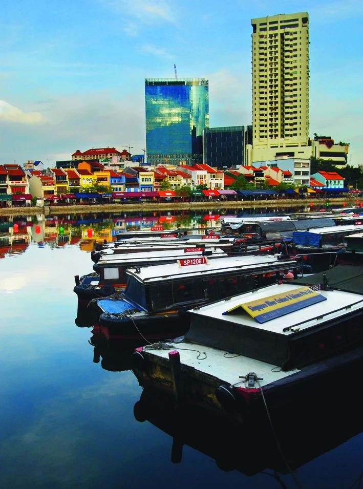 Several long passenger boats are moored beside colourful riverside buildings.