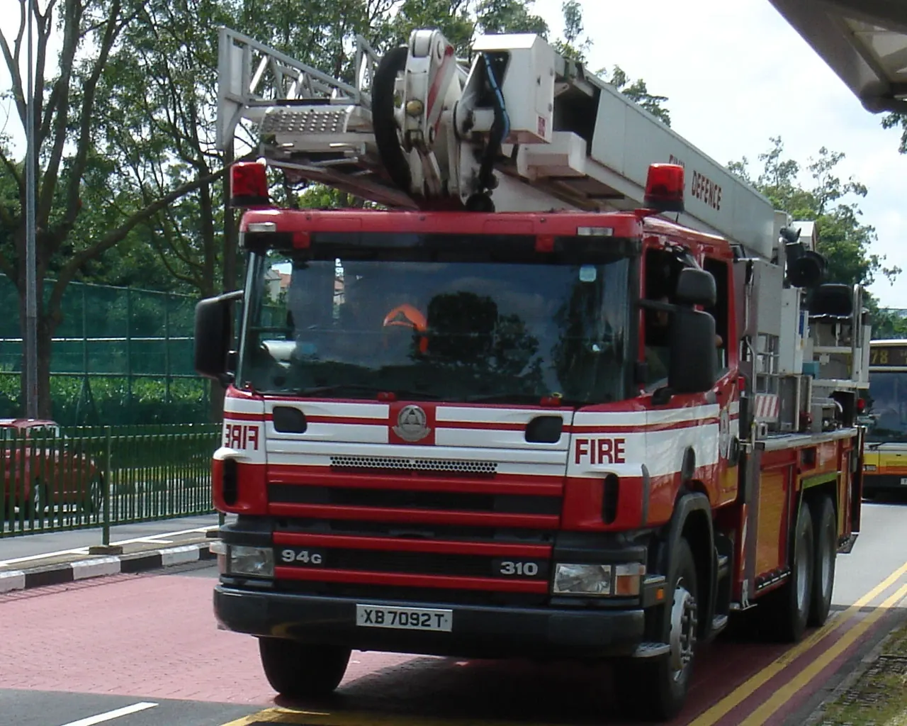 A red-and-white ladder truck has a long grey arm folded over its roof.