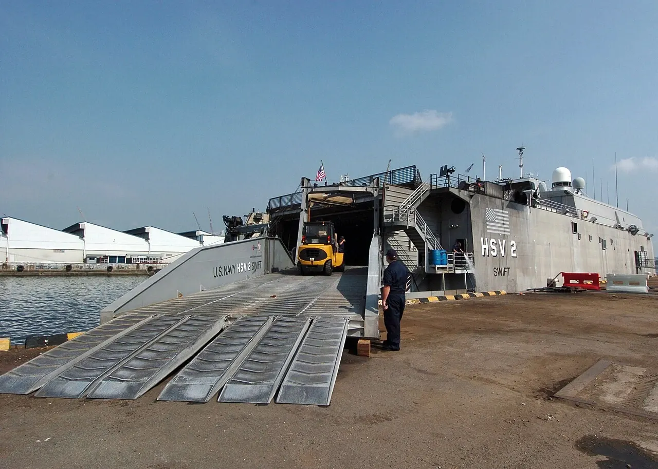 A small yellow forklift stands on a wide loading ramp leading into a ship.