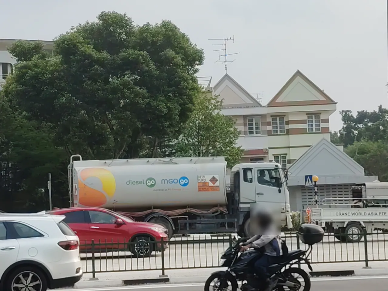 A white tanker with a long round barrel drives past terraced houses.