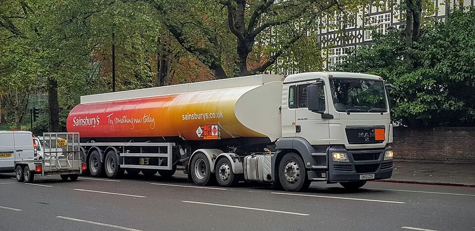 A white truck pulls a long fuel tank painted in orange, yellow and white.