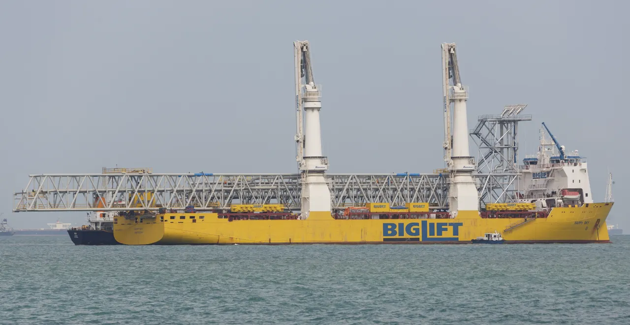 A yellow heavy-lift ship carries two tall white cranes and a long metal framework.