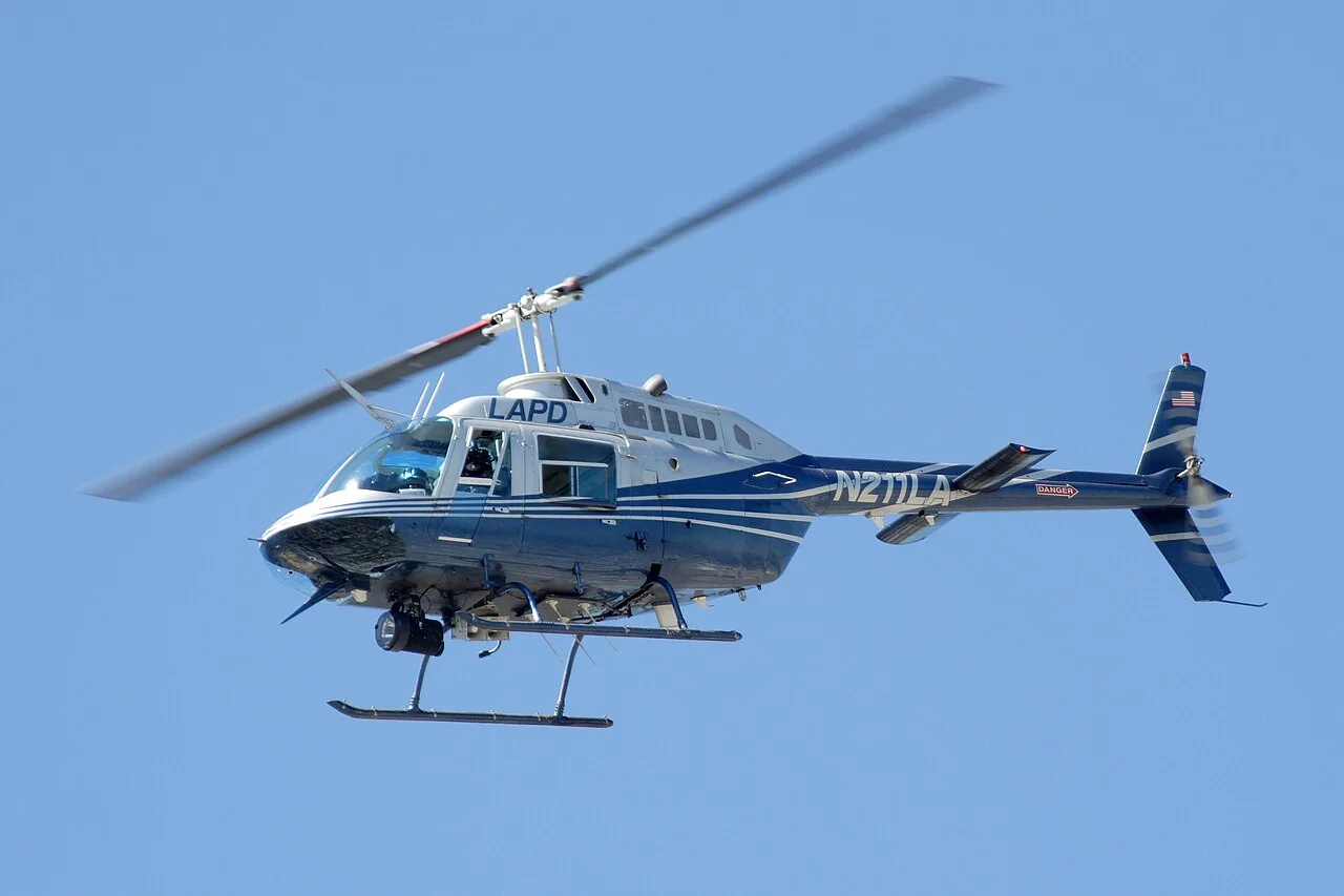 A blue and white LAPD helicopter flies against a clear blue sky.