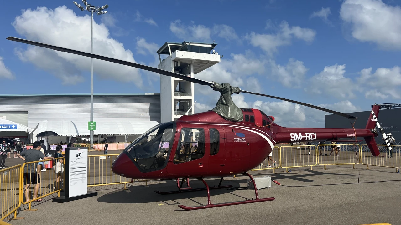 A red helicopter stands on skids behind yellow barriers at an airshow.