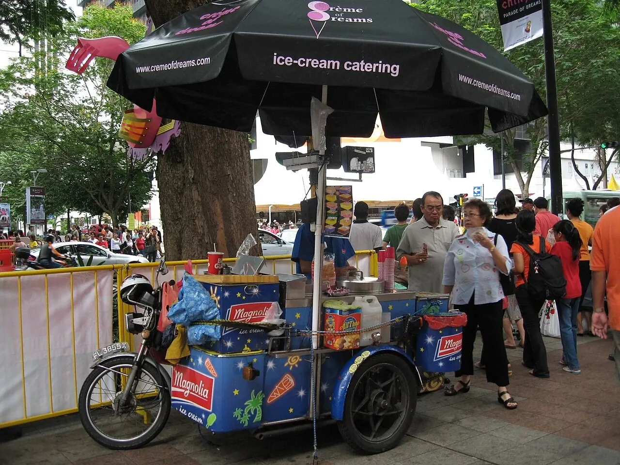 A blue ice-cream sidecar stands beside a motorcycle under a large black umbrella.