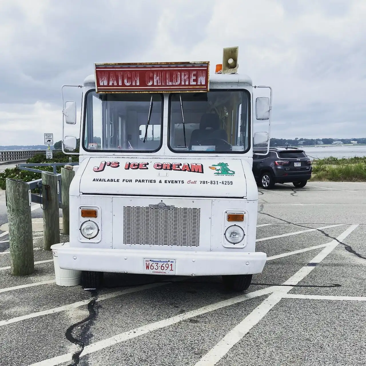 An ice-cream truck has a large front window and a sign above it.