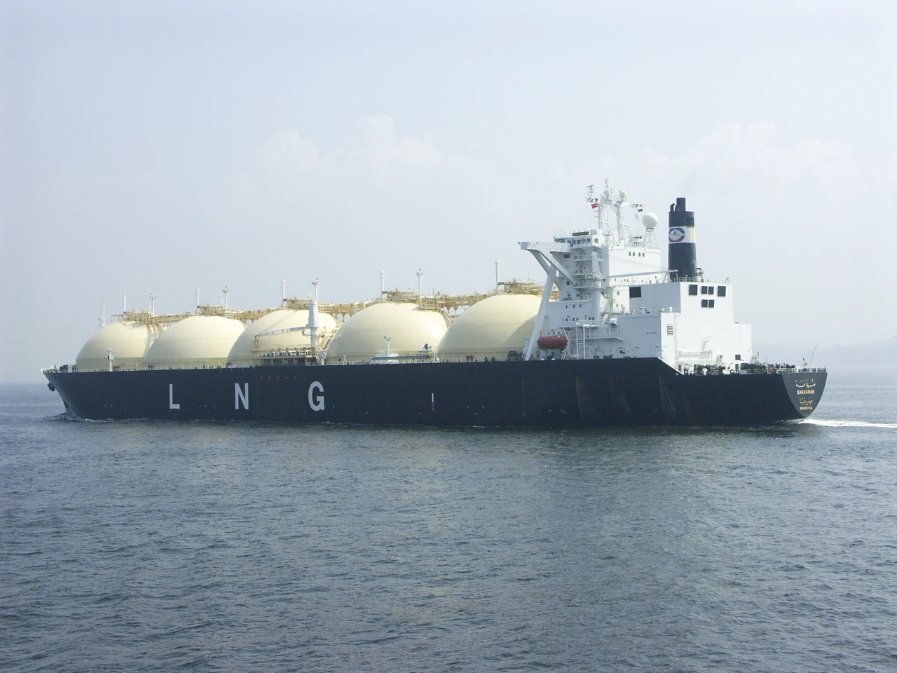 A black and white LNG carrier has four large round tanks along its deck.