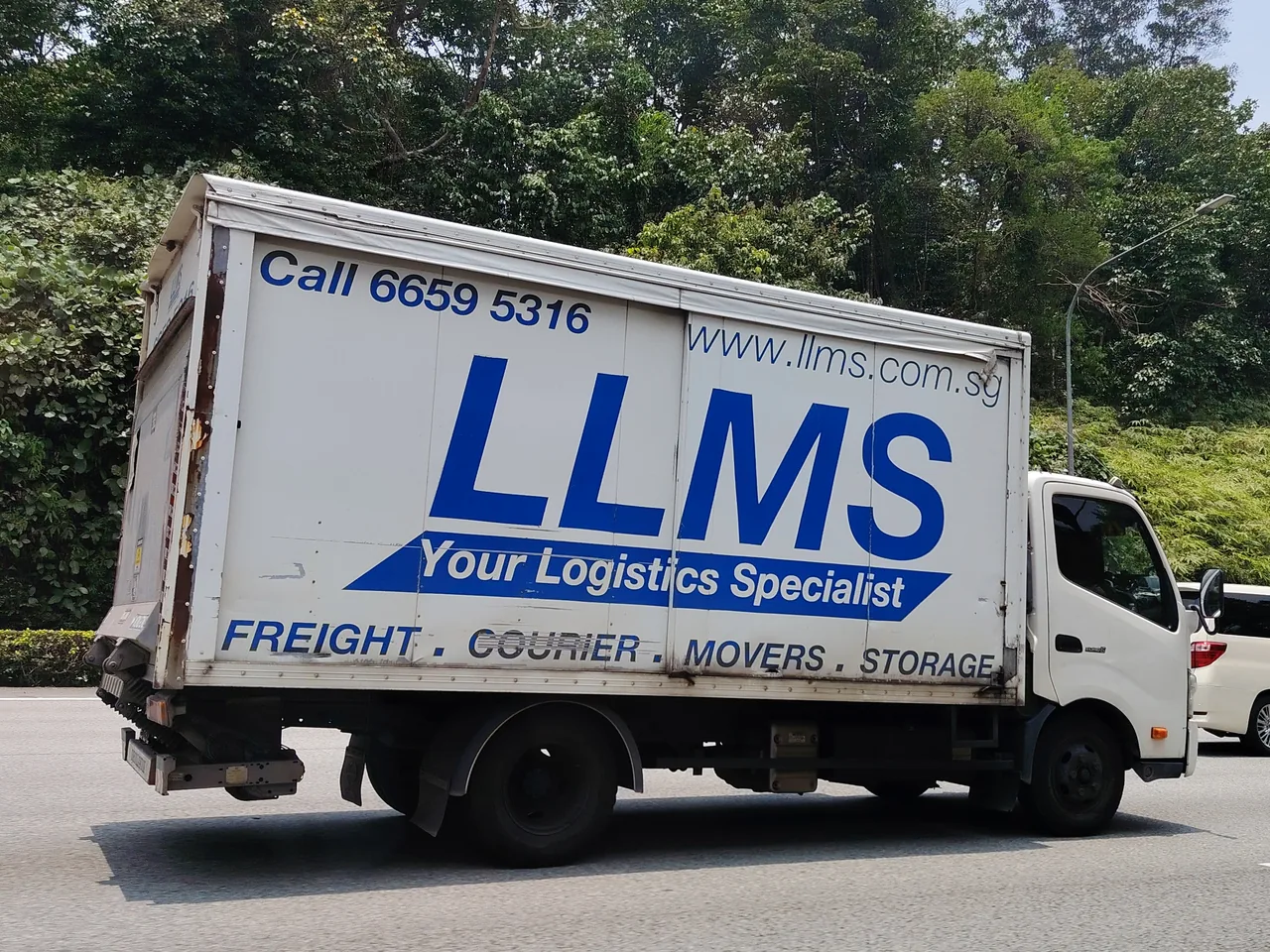 Lorry — a white box lorry with blue lettering and a tail lift folded up at the back, Photographed in Singapore
