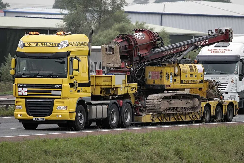 A yellow truck pulls a low trailer carrying a large tracked machine.