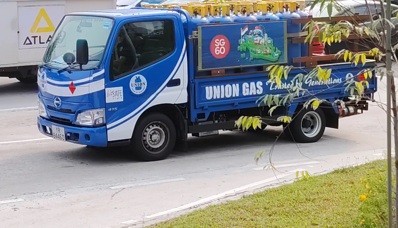 A blue-and-white lorry carries two rows of blue gas cylinders with yellow guards.