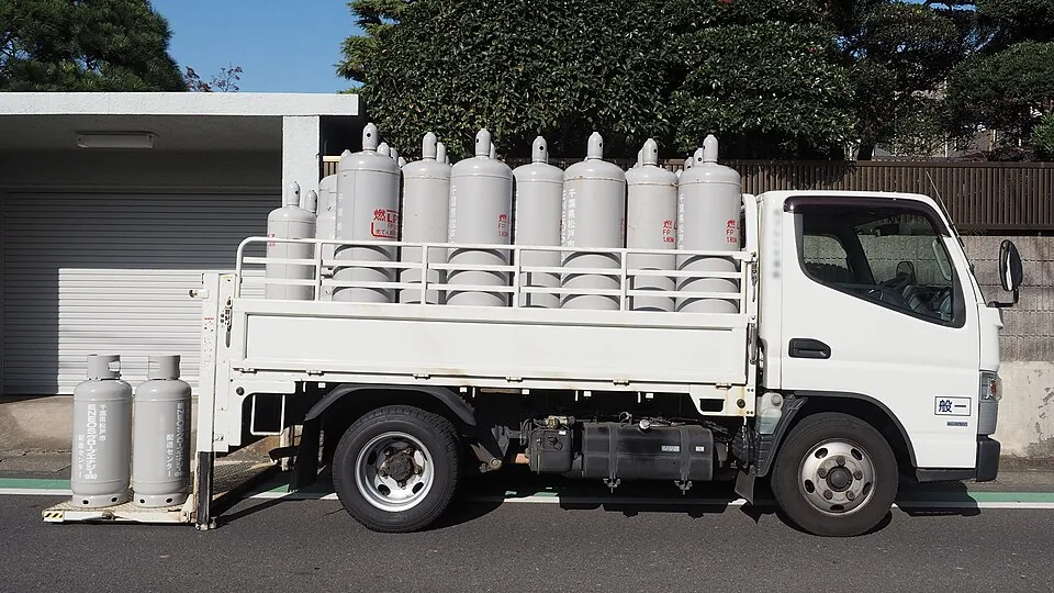 A white truck carries upright silver gas cylinders behind low side panels.