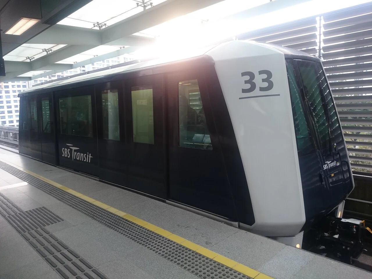 A black and white SBS Transit LRT train numbered 33 is stopped at a station platform.