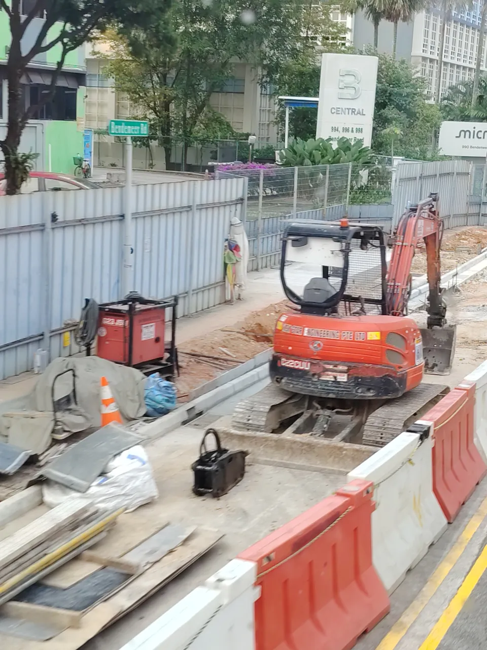Mini excavator — a small orange excavator on rubber tracks, digging beside the road, Photographed in Singapore