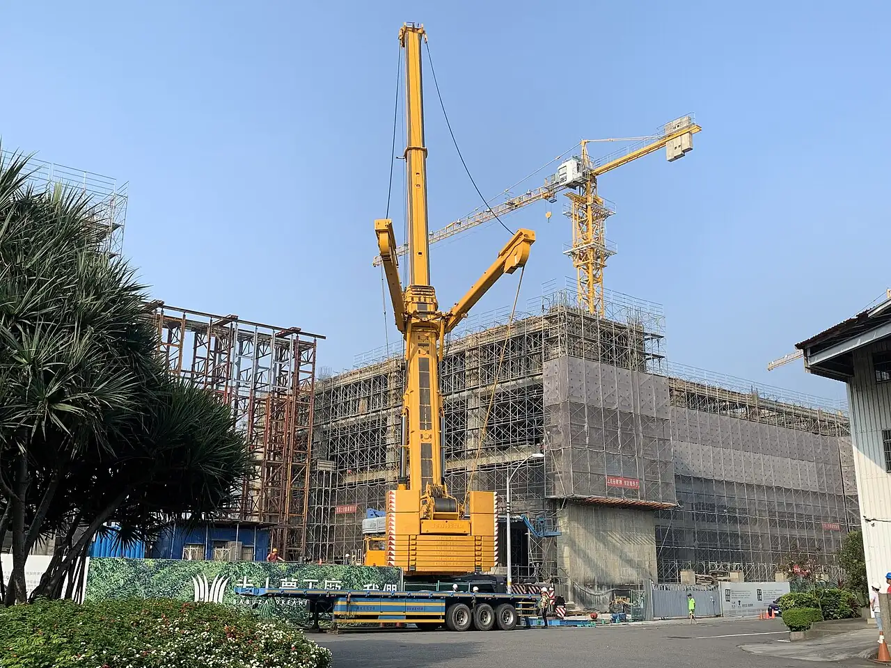 A yellow mobile crane raises its long boom beside a building site.
