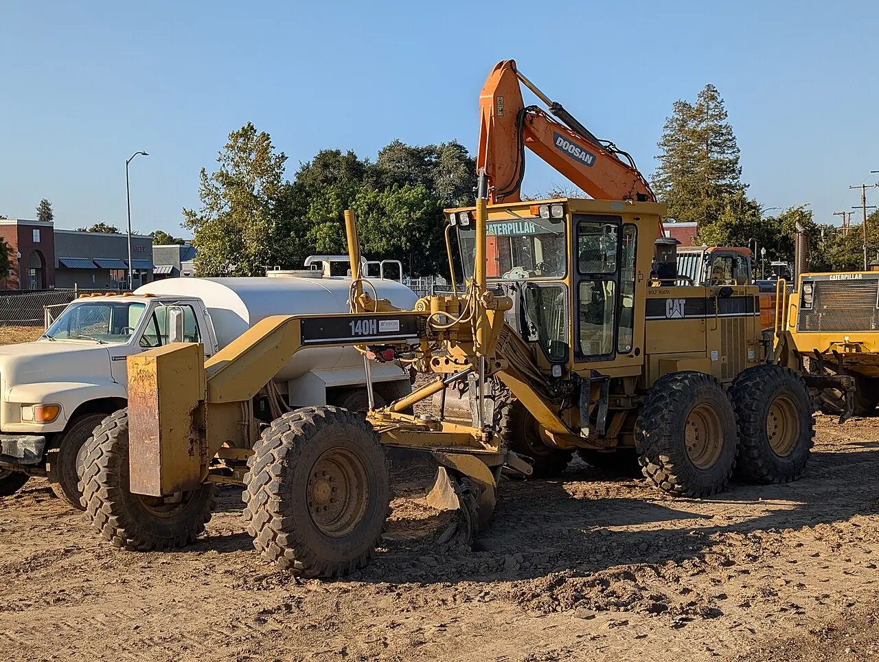 A yellow grader has a long body and a blade between its front and rear wheels.