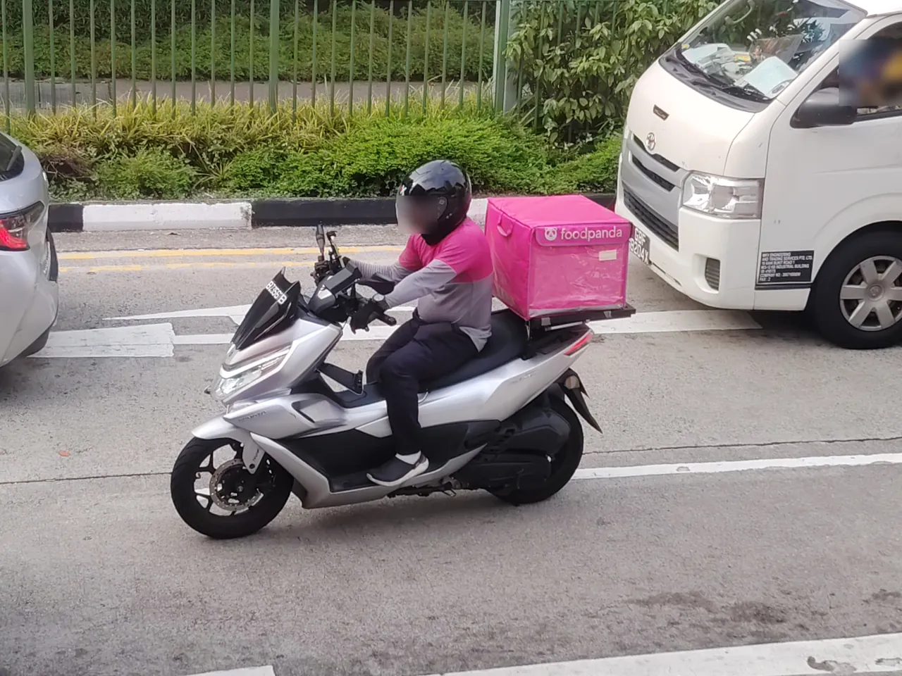 Motorcycle — a delivery rider on a silver scooter with a bright pink food box behind him, photographed in Singapore.