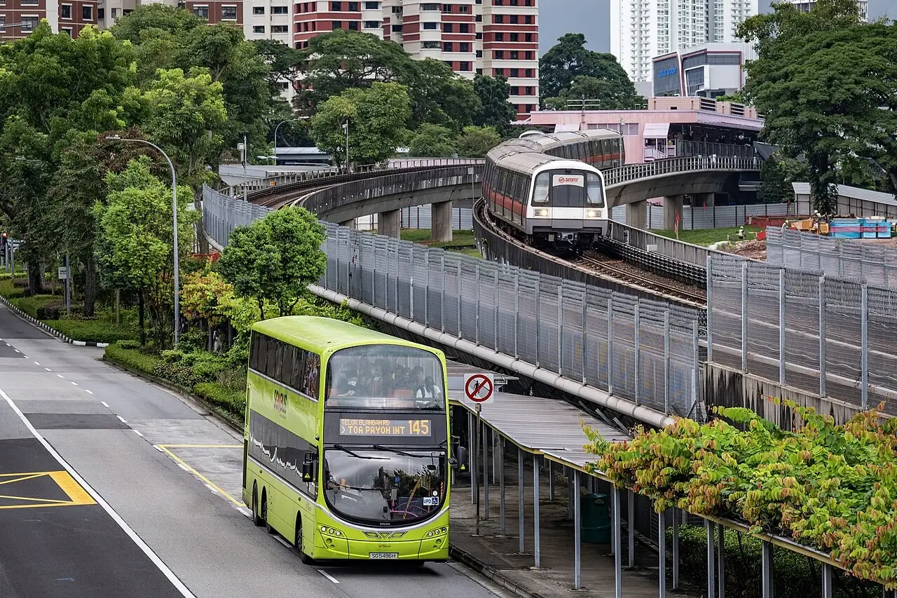 An MRT train on raised tracks appears above a green double-decker bus.