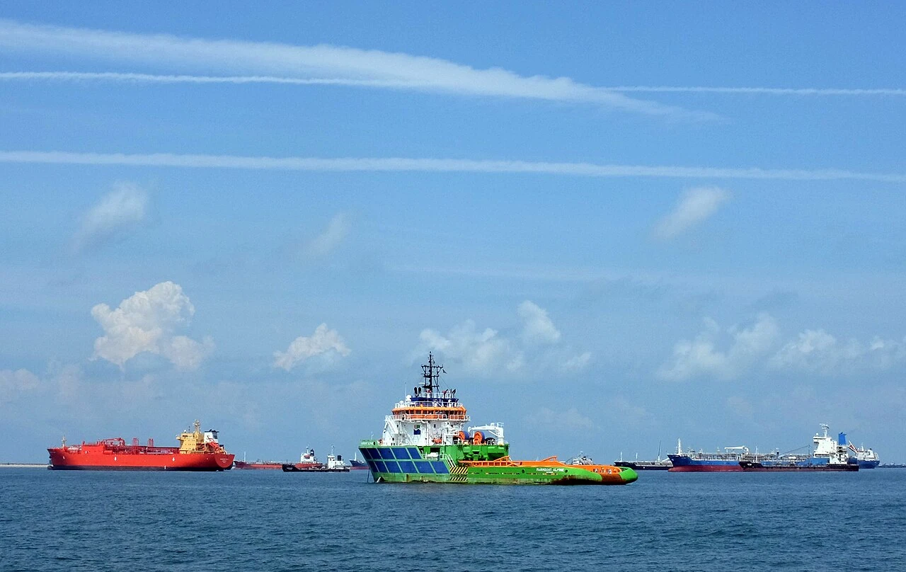 A green-and-blue support ship has a tall white front and a long low rear deck.