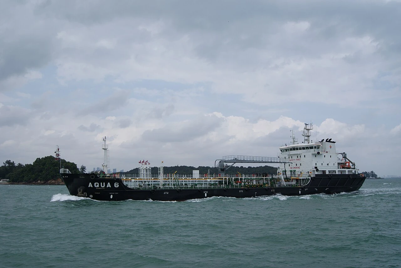 A black-and-white tanker has pipes along its low deck.