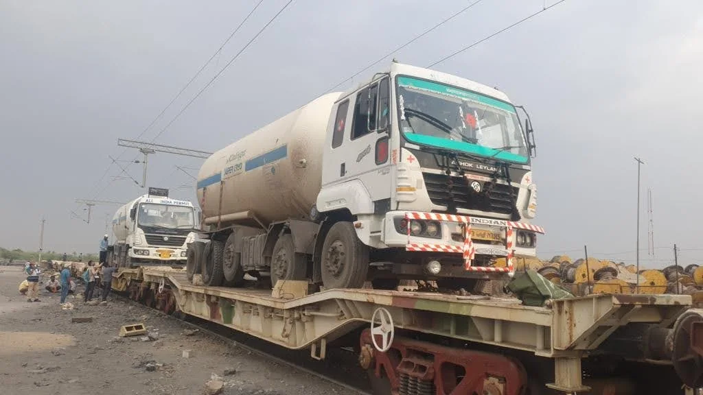 A tanker truck with a rounded tank is secured on a railway flatbed wagon.