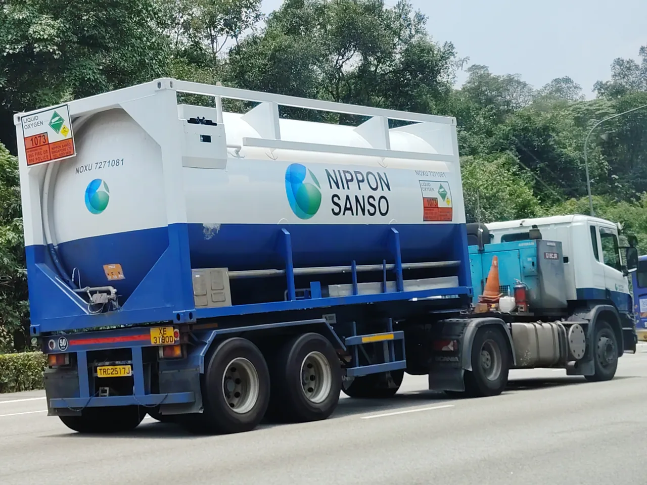Oxygen tanker — a white and blue round tank inside a white frame on a blue trailer pulled by a white lorry, Photographed in Singapore