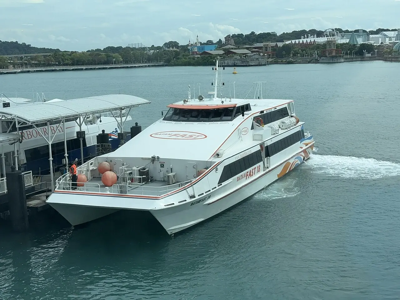 A white passenger catamaran waits beside a jetty, with windows along its enclosed deck.