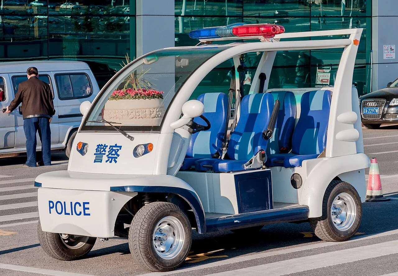 An open-sided police buggy with blue seats is parked at an airport entrance.