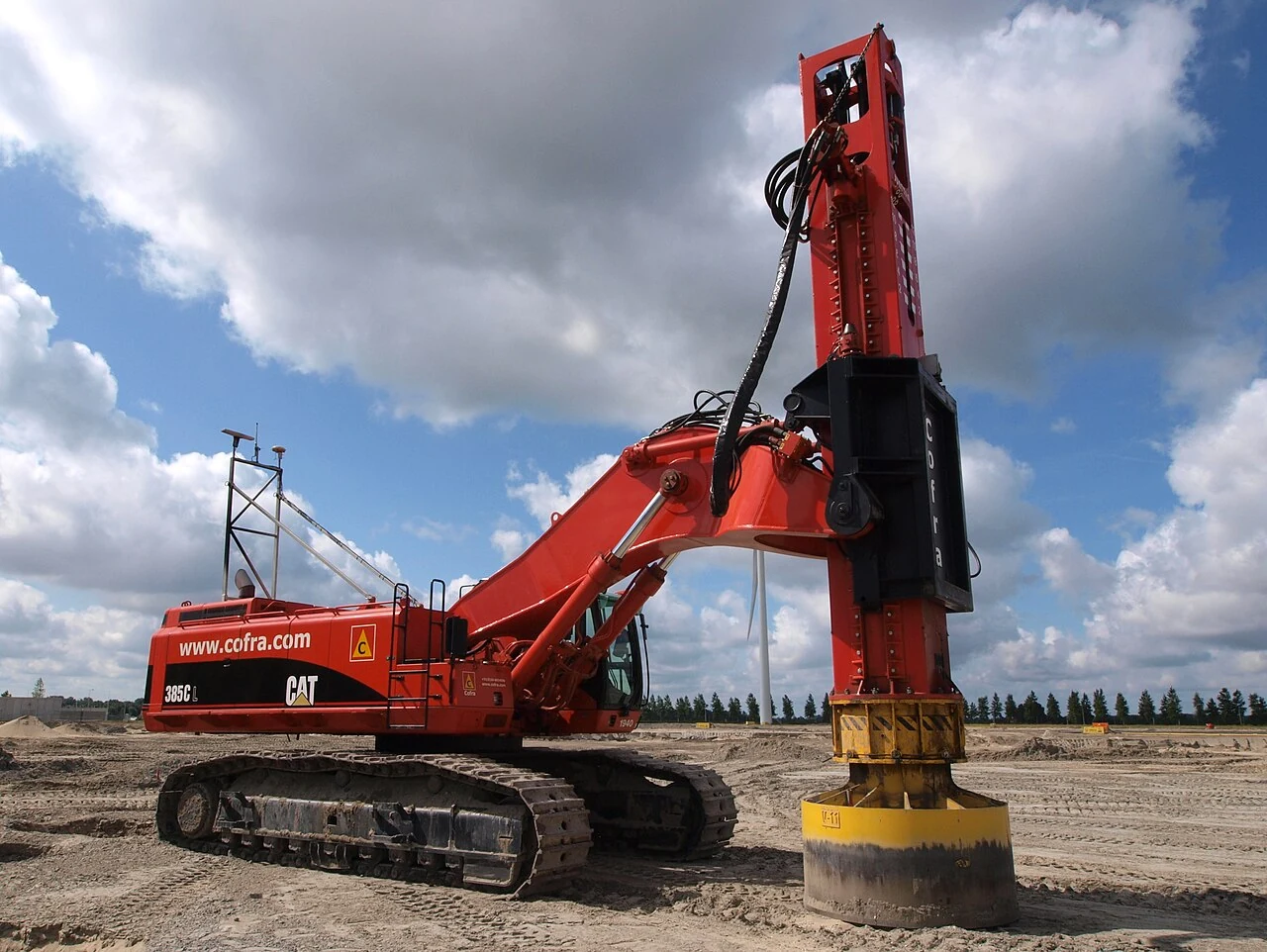 A red tracked piling machine with a tall pile-driving mast.