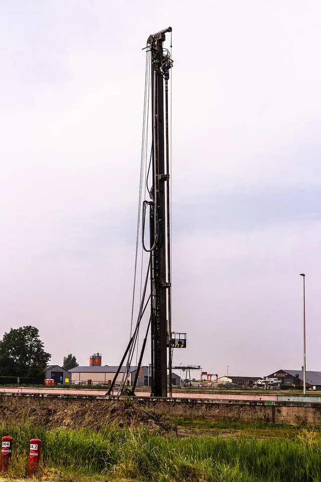 A piling rig has a tall straight mast rising above its small tracked base.