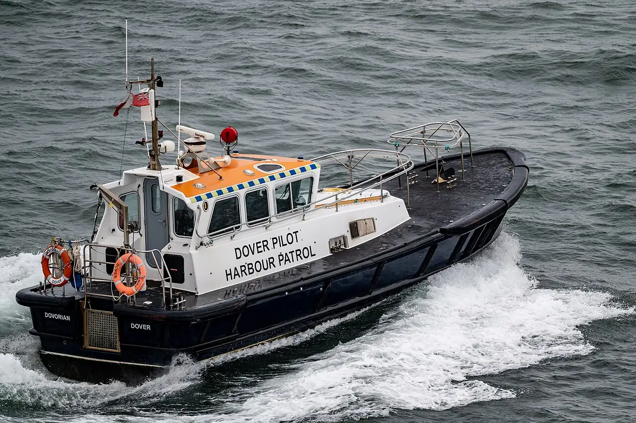A black-and-white pilot boat travels quickly across choppy water, leaving a white wake behind it.